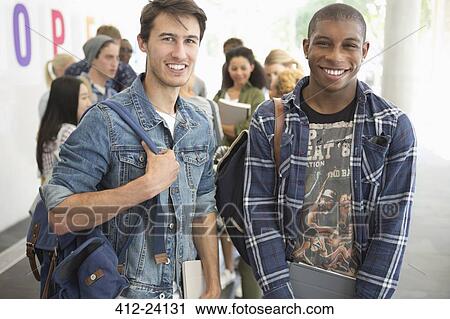 Stock Image - Two male students smiling at camera with other students in background. Fotosearch