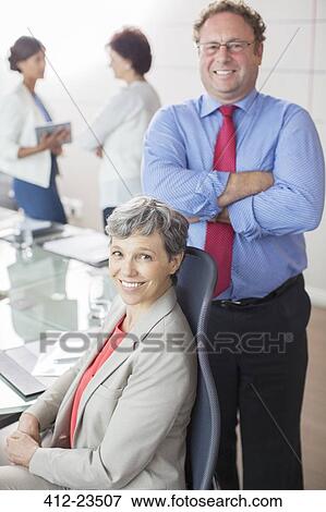 Stock Photo - Two mature business people looking at camera, smiling in conference room. Fotosearch