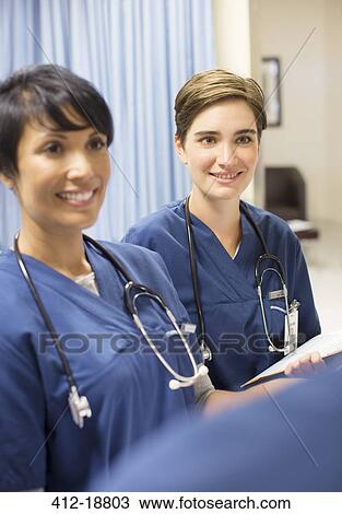 Stock Image - Two smiling doctors wearing scrubs with stethoscopes around necks in hospital. Fotosearch
