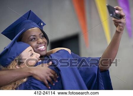 Two smiling female students taking selfie at graduation View Large Photo Image Picture - Two smiling female students taking selfie at graduation. Fotosearch