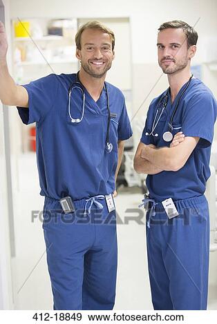 Two smiling male doctors wearing scrubs standing in hospital ward View Large Photo Image Stock Photo - Two smiling male doctors wearing scrubs standing in hospital ward. Fotosearch