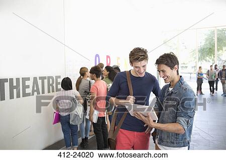 Stock Image - Two university friends looking at tablet in corridor. Fotosearch