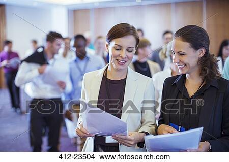 Picture - Two young businesswoman looking through files in conference room. Fotosearch