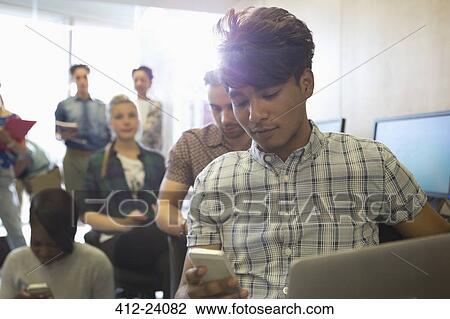 Stock Image - University students texting during break in classroom. Fotosearch