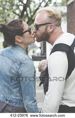 View of couple in sunglasses kissing and holding baby in city streets View Large Photo Image Stock Photograph - View of couple in sunglasses kissing and holding baby in city streets. Fotosearch