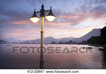 Stock Photo - View of illuminated street light with bay and mountains in background . Fotosearch