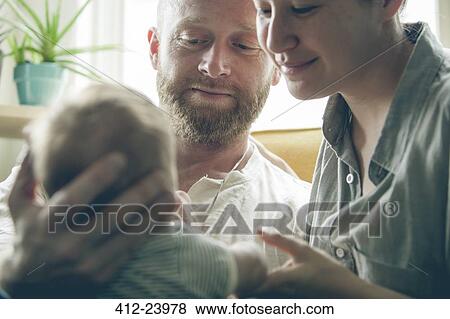View of parents smiling and holding little baby, sitting beside window View Large Photo Image Stock Photo - View of parents smiling and holding little baby, sitting beside window. Fotosearch