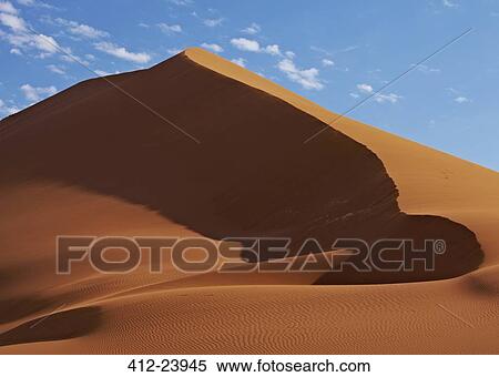 Stock Photography - View of sand dunes in desert with blue sky and clouds in background. Fotosearch