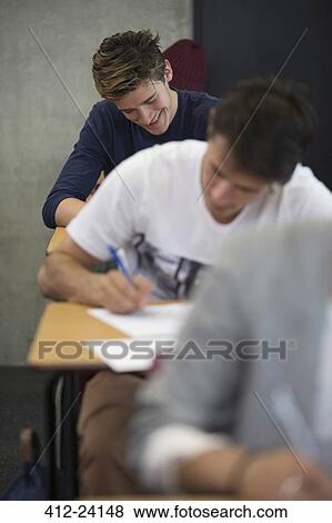 Stock Photo - View of smiling students sitting at desks during an exam in classroom. Fotosearch