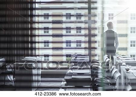 Stock Photograph - Young businessman standing in conference room looking out of window. Fotosearch