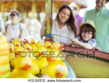 Stock Image - Boy trying to catch rubber duck on fishing game in amusement park. Fotosearch