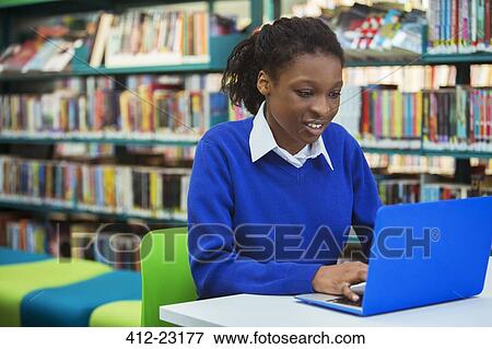 Stock Photo - Busy female student with laptop in library. Fotosearch