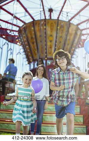 Stock Photo - Children running in front of carousel, mother following them. Fotosearch