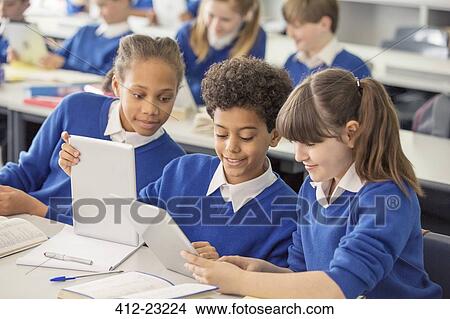 Elementary school children wearing blue school uniforms using digital tablets at desk in classroom View Large Photo Image Picture - Elementary school children wearing blue school uniforms using digital tablets at desk in classroom. Fotosearch