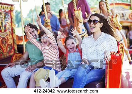 Stock Image - Family on carousel in amusement park. Fotosearch