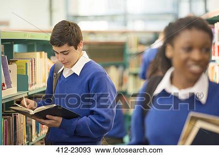 Stock Image - Female and male teenage students holding books in school library. Fotosearch