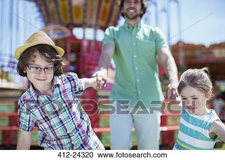 Stock Image - Girl and boy pulling their father in amusement park. Fotosearch