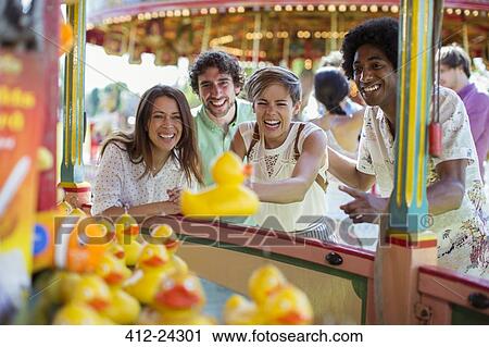 Stock Image - Group of friends having fun with fishing game in amusement park. Fotosearch