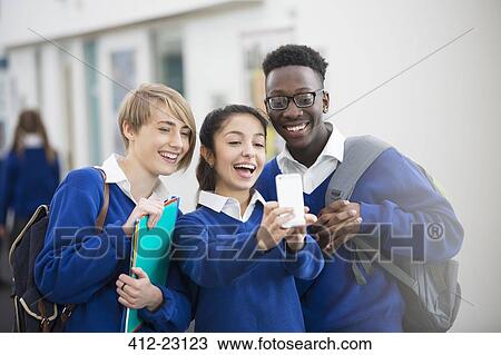 Stock Image - Happy students wearing school uniforms using smartphone in school corridor. Fotosearch