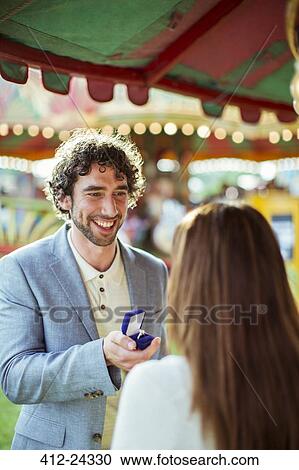 Stock Image - Man proposing to girlfriend in amusement park. Fotosearch