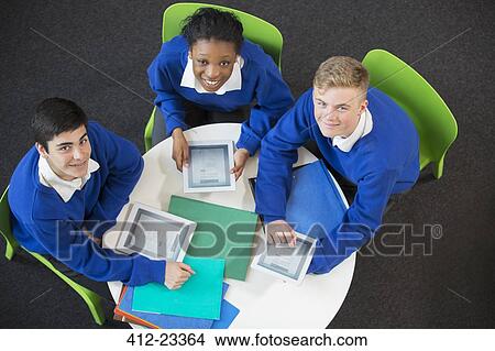 Overhead portrait of three students with digital tablets sitting together at round table View Large Photo Image Picture - Overhead portrait of three students with digital tablets sitting together at round table. Fotosearch