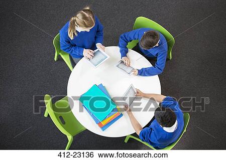 Stock Photograph - Overhead view of boys and girl sitting at round table and using digital tablets. Fotosearch