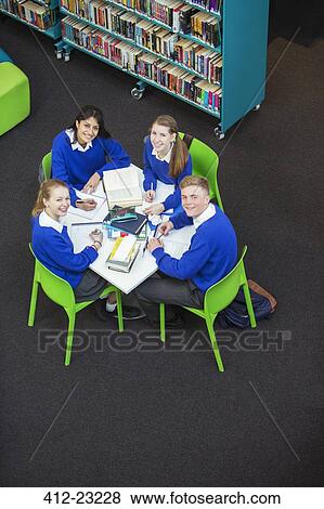 Overhead view of four students doing their homework at round table, looking at camera View Large Photo Image Stock Photo - Overhead view of four students doing their homework at round table, looking at camera. Fotosearch