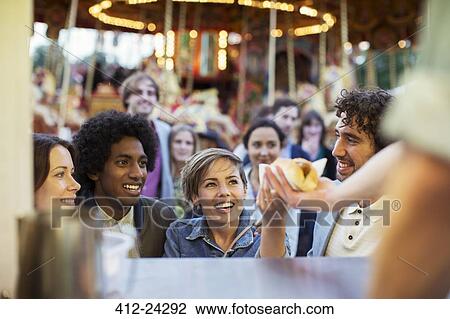Stock Image - People buying hot dogs in food stand in amusement park. Fotosearch
