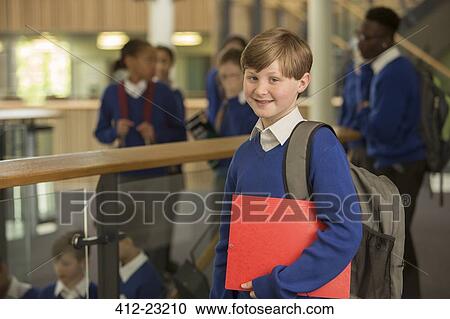 Stock Image - Portrait of elementary school boy wearing blue school uniform standing in school corridor. Fotosearch