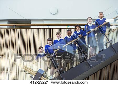 Stock Image - Portrait of elementary school children wearing blue school uniforms standing on steps in school. Fotosearch