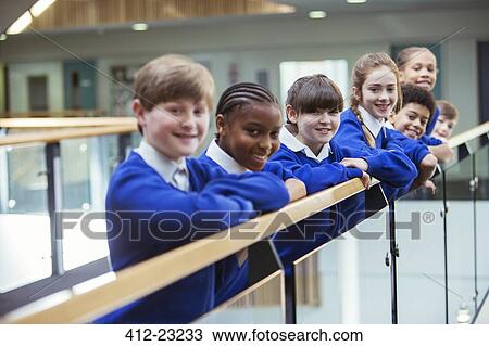 Stock Image - Portrait of elementary school children wearing blue school uniforms standing in school corridor. Fotosearch