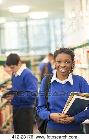 Stock Photograph - Portrait of female high school student with books in library. Fotosearch