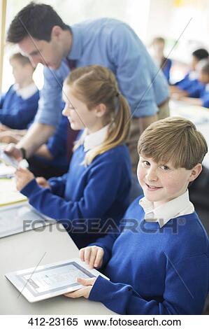 Portrait of schoolboy sitting with digital tablet in classroom, children and teacher in background View Large Photo Image Stock Photography - Portrait of schoolboy sitting with digital tablet in classroom, children and teacher in background. Fotosearch