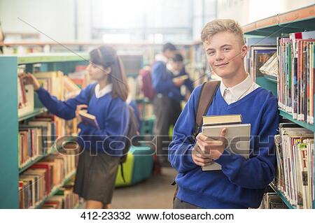 Portrait of smiling male student wearing blue school uniform holding books in library View Large Photo Image Stock Image - Portrait of smiling male student wearing blue school uniform holding books in library. Fotosearch