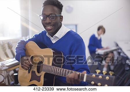 Portrait of smiling male student playing acoustic guitar in classroom View Large Photo Image Stock Photo - Portrait of smiling male student playing acoustic guitar in classroom. Fotosearch