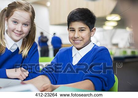 Picture - Portrait of smiling school children wearing blue school uniforms sitting at desk. Fotosearch