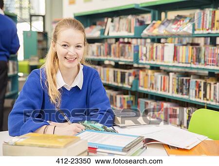 Stock Image - Portrait of smiling schoolgirl doing homework in library. Fotosearch