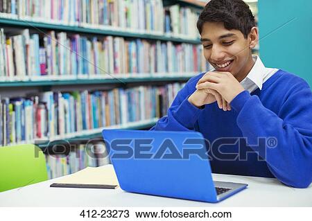 Stock Image - Portrait of student smiling and looking at laptop in library. Fotosearch