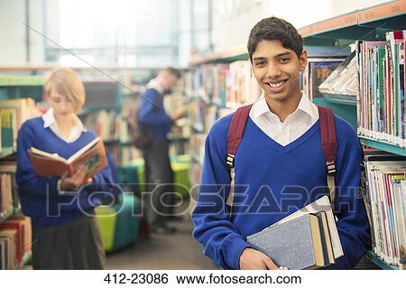 Stock Photograph - Portrait of teenage student standing with books in college library. Fotosearch
