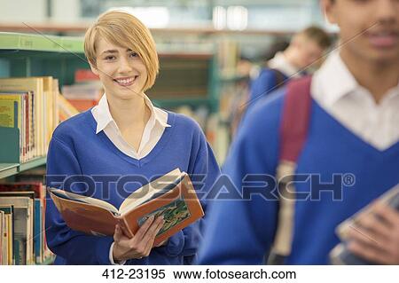 Stock Photography - Portrait of teenage student standing with book in library. Fotosearch