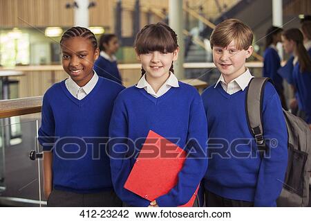 Stock Image - Portrait of three elementary school children wearing blue school uniforms standing in corridor. Fotosearch