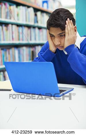 Portrait of worried student looking on laptop in library View Large Photo Image Stock Photo - Portrait of worried student looking on laptop in library. Fotosearch