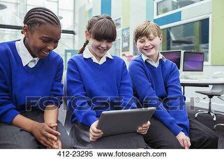 Primary school children wearing blue school uniforms holding digital tablet and smiling in classroom View Large Photo Image Stock Photography - Primary school children wearing blue school uniforms holding digital tablet and smiling in classroom. Fotosearch