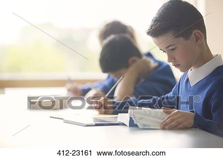 Stock Image - Pupil learning in classroom using book and tablet pc. Fotosearch