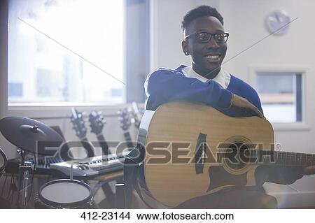 Smiling college student sitting with acoustic guitar in classroom View Large Photo Image Picture - Smiling college student sitting with acoustic guitar in classroom. Fotosearch