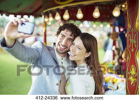 Smiling couple taking selfie in amusement park View Large Photo Image Stock Photograph - Smiling couple taking selfie in amusement park. Fotosearch