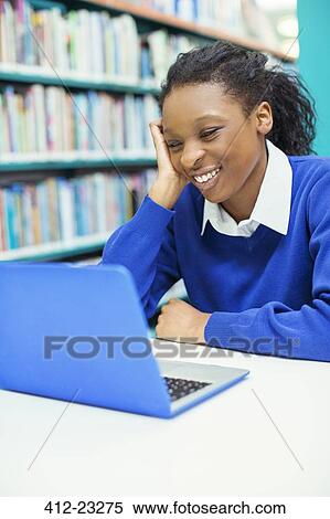 Smiling female student looking at laptop in library View Large Photo Image Stock Photography - Smiling female student looking at laptop in library. Fotosearch