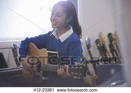 Stock Image - Smiling female student playing acoustic guitar. Fotosearch