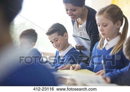 Stock Photograph - Smiling female teacher with his pupils in classroom. Fotosearch