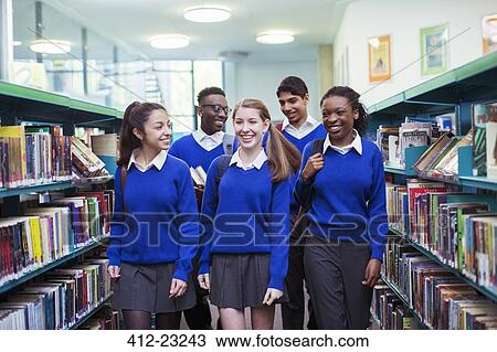 Smiling students wearing blue school uniforms walking between bookshelves in library View Large Photo Image Stock Image - Smiling students wearing blue school uniforms walking between bookshelves in library. Fotosearch